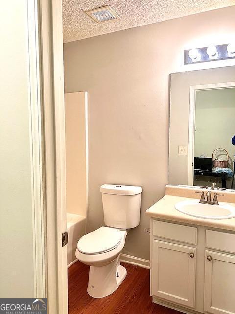 bathroom featuring hardwood / wood-style flooring, vanity, a textured ceiling, and toilet