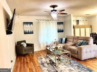 living room with ceiling fan, wood-type flooring, and a textured ceiling