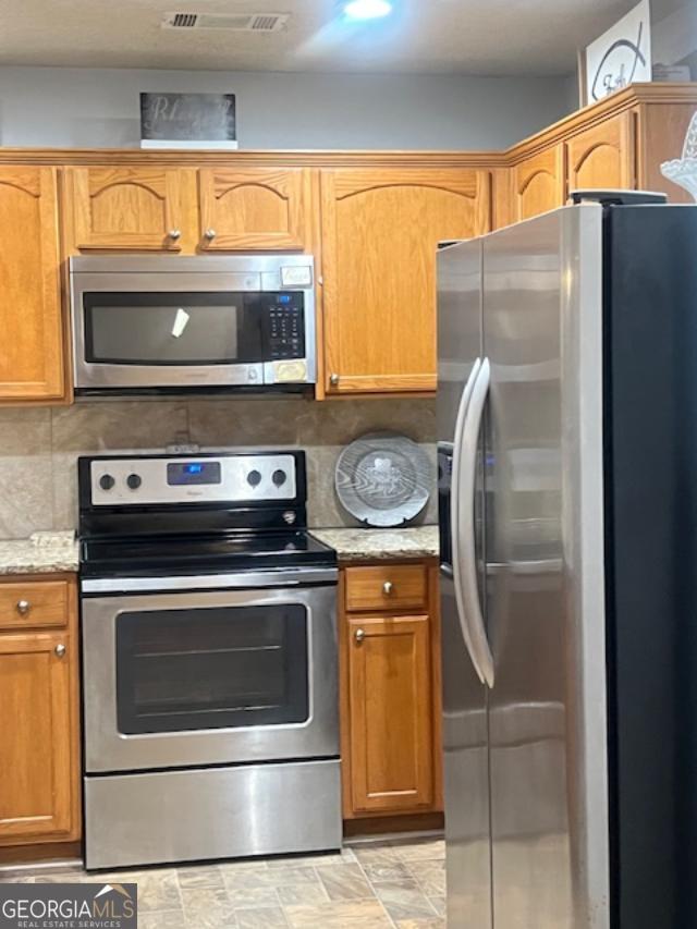 kitchen featuring tasteful backsplash, stainless steel appliances, and light stone counters