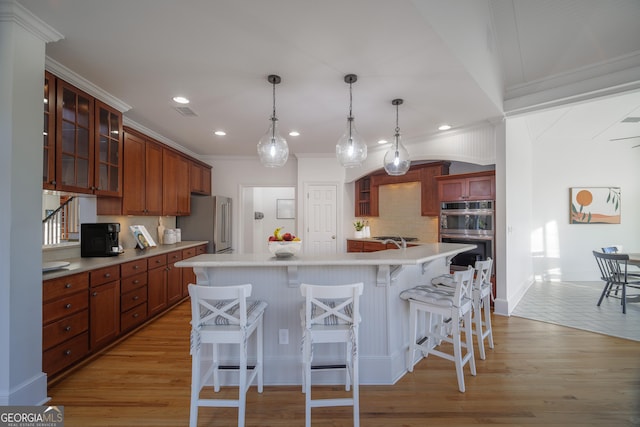 kitchen featuring a breakfast bar area, light hardwood / wood-style flooring, ornamental molding, appliances with stainless steel finishes, and a kitchen island with sink