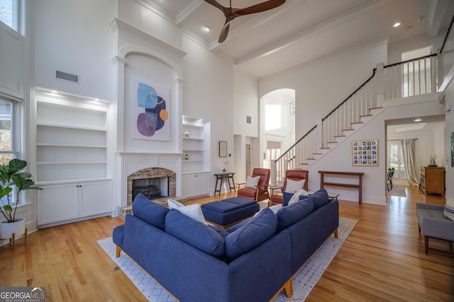 living room with a stone fireplace, light hardwood / wood-style flooring, ornamental molding, and a high ceiling