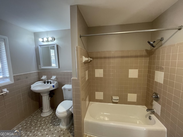 bathroom with toilet, tiled shower / bath combo, tile patterned flooring, and tile walls