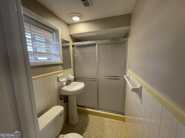 bathroom featuring toilet, a shower with shower door, and tile walls