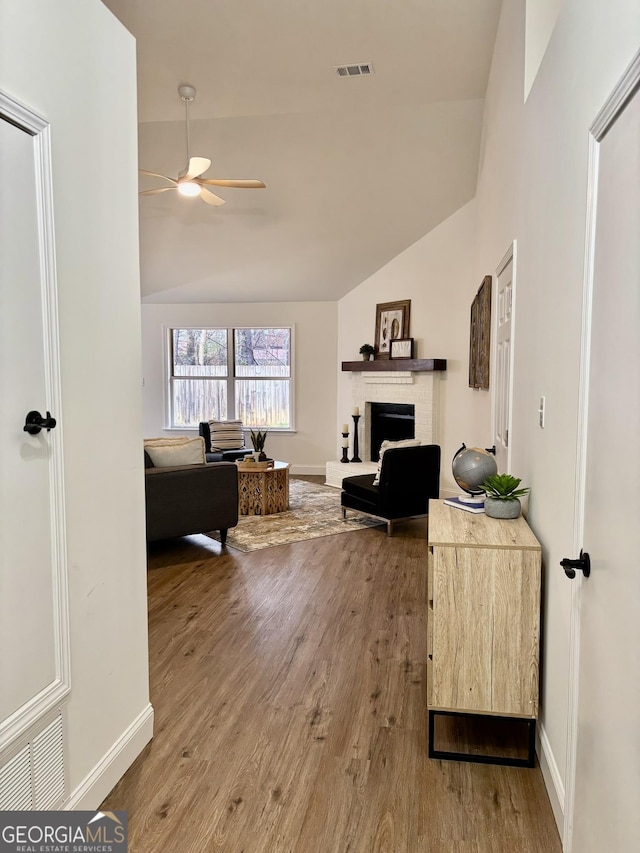 living room with wood-type flooring, lofted ceiling, ceiling fan, and a brick fireplace