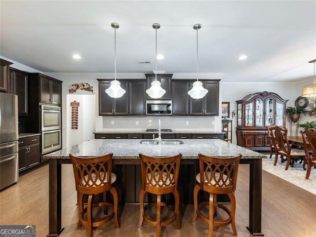 kitchen with hanging light fixtures, stainless steel appliances, sink, and a center island with sink