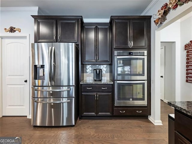 kitchen with appliances with stainless steel finishes, dark stone countertops, backsplash, dark hardwood / wood-style flooring, and crown molding