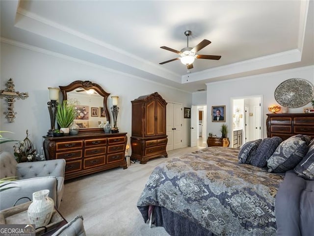 carpeted bedroom with a raised ceiling, crown molding, connected bathroom, and ceiling fan