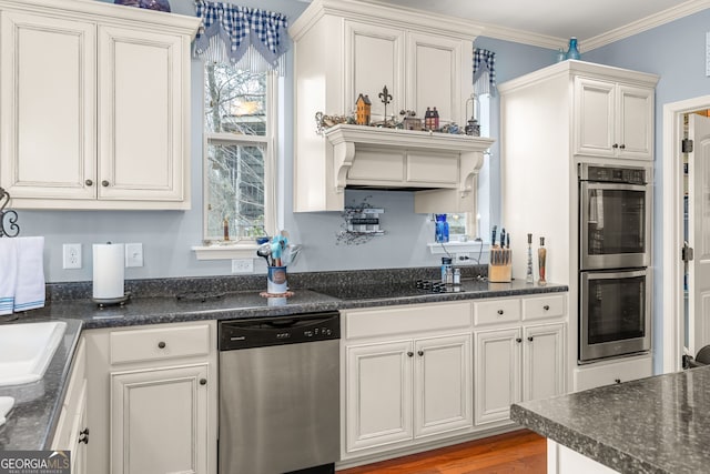 kitchen with wood-type flooring, white cabinets, dark stone counters, stainless steel appliances, and crown molding