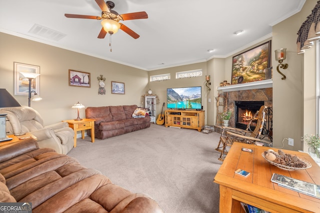 carpeted living room featuring a stone fireplace, ornamental molding, and ceiling fan