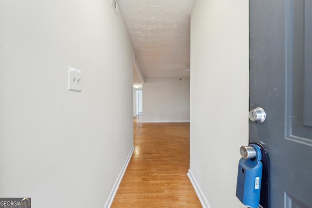 hallway featuring a textured ceiling, light wood-type flooring, and baseboards