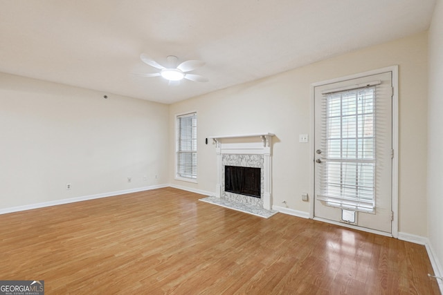 unfurnished living room with a ceiling fan, light wood-type flooring, baseboards, and a premium fireplace