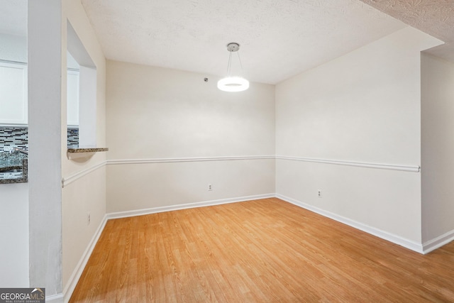 unfurnished dining area with a textured ceiling, light wood finished floors, and baseboards