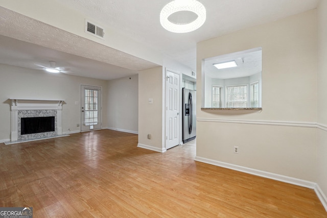 unfurnished living room with light wood-type flooring, a premium fireplace, baseboards, and a ceiling fan