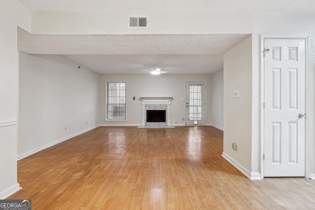 unfurnished living room with light wood finished floors, a fireplace, visible vents, and a healthy amount of sunlight