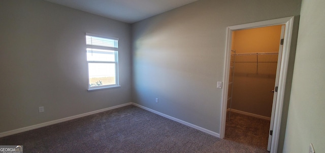 unfurnished bedroom with multiple windows, a walk in closet, and carpet flooring