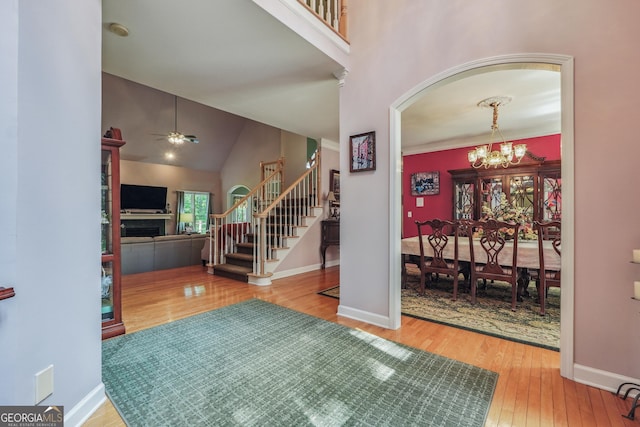 foyer entrance with ceiling fan with notable chandelier, wood-type flooring, and high vaulted ceiling