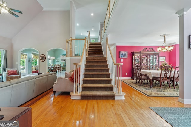 staircase featuring hardwood / wood-style floors, ceiling fan with notable chandelier, and high vaulted ceiling