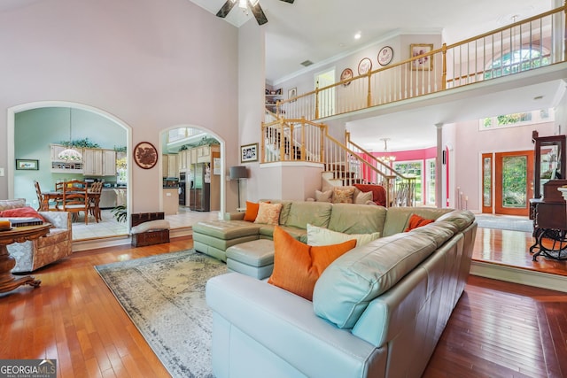 living room with crown molding, ceiling fan with notable chandelier, hardwood / wood-style floors, and a high ceiling