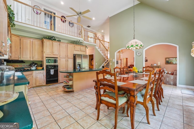 tiled dining room featuring ceiling fan, ornamental molding, and a high ceiling