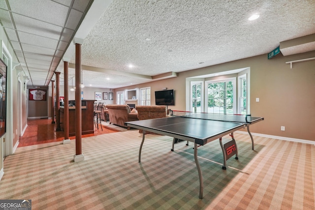 rec room with bar, light colored carpet, a textured ceiling, and a drop ceiling