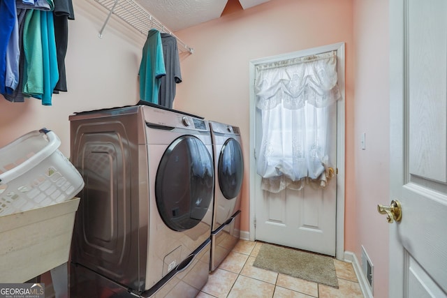 clothes washing area featuring light tile patterned floors, washing machine and clothes dryer, and a textured ceiling