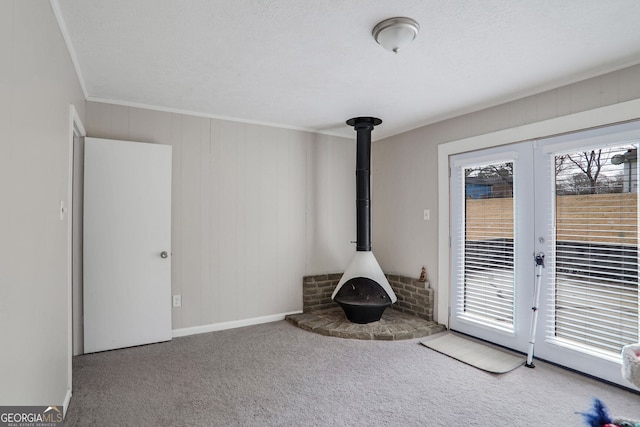 unfurnished living room featuring french doors, carpet flooring, crown molding, baseboards, and a wood stove