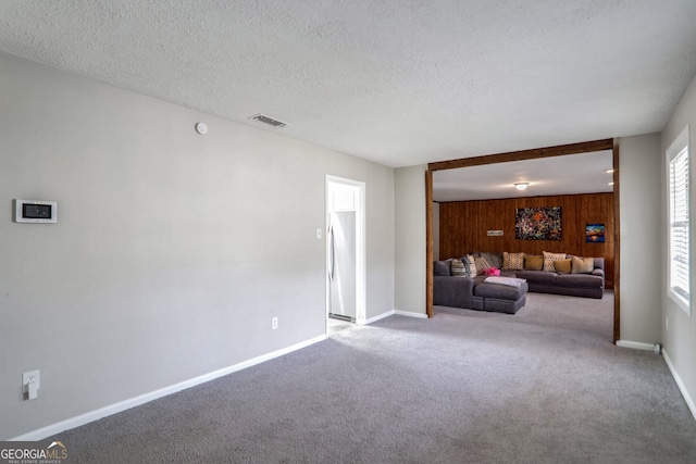 unfurnished living room featuring wooden walls, carpet, baseboards, visible vents, and a textured ceiling