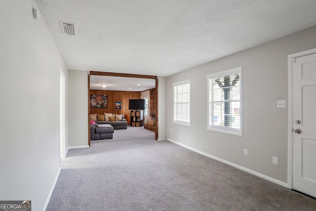 unfurnished living room featuring visible vents, wood walls, a textured ceiling, and carpet floors