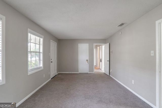 empty room featuring baseboards, visible vents, carpet floors, and a textured ceiling