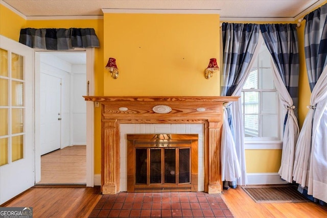 unfurnished living room with hardwood / wood-style flooring, crown molding, and a tiled fireplace