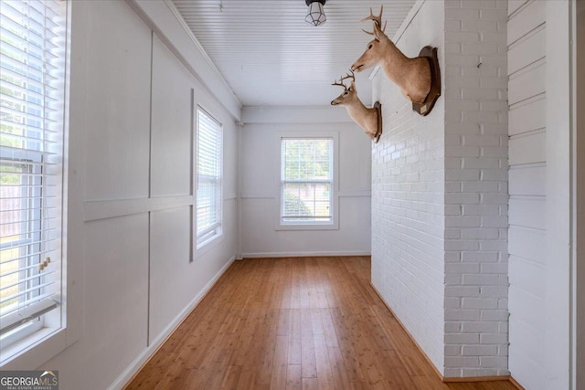 unfurnished room with ornamental molding, brick wall, and light wood-type flooring