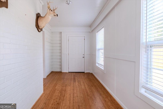 hallway with ornamental molding, brick wall, a healthy amount of sunlight, and light wood-type flooring