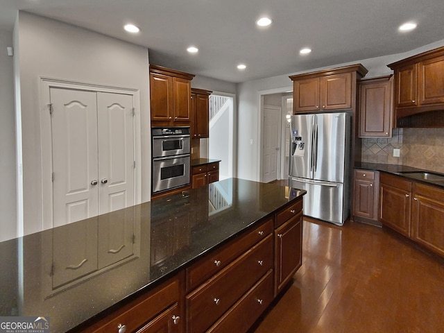 kitchen featuring sink, dark stone countertops, dark hardwood / wood-style flooring, stainless steel appliances, and backsplash