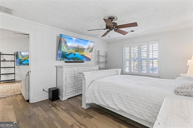 bedroom with a textured ceiling, wood-type flooring, ornamental molding, and ceiling fan