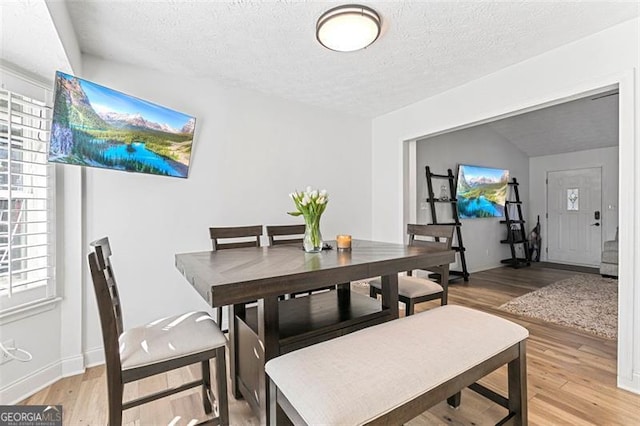 dining area with vaulted ceiling, a textured ceiling, and light hardwood / wood-style flooring