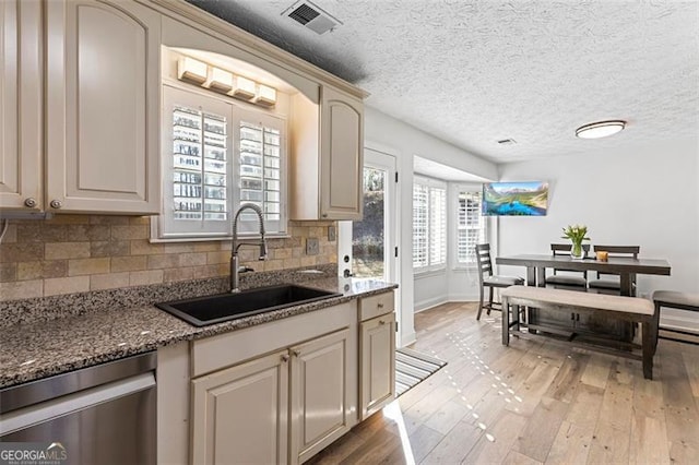 kitchen with sink, dishwasher, cream cabinetry, dark stone counters, and light wood-type flooring