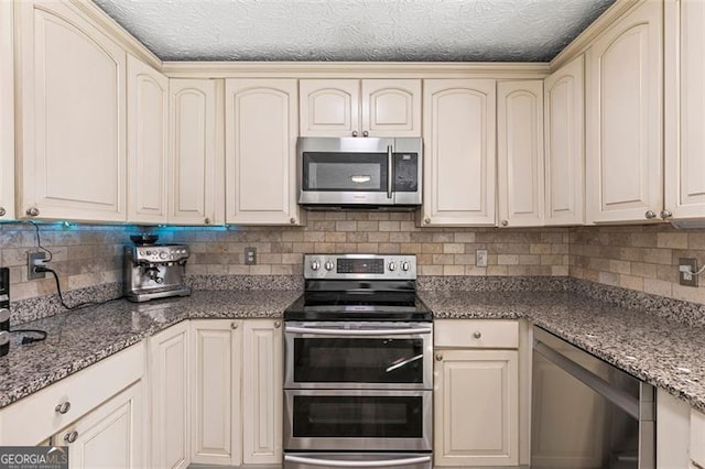 kitchen featuring tasteful backsplash, cream cabinetry, dark stone counters, and appliances with stainless steel finishes