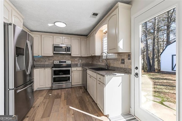 kitchen with sink, stone counters, stainless steel appliances, a textured ceiling, and dark hardwood / wood-style flooring