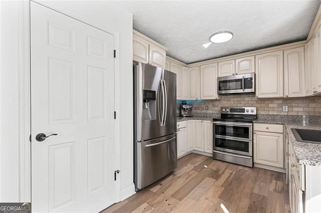 kitchen with tasteful backsplash, a textured ceiling, light wood-type flooring, stainless steel appliances, and cream cabinetry