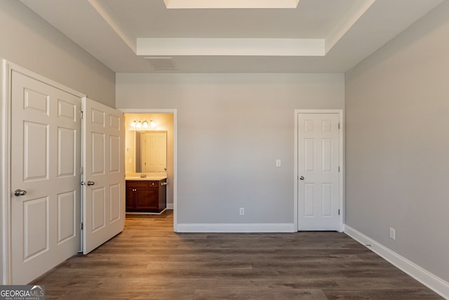 unfurnished bedroom with connected bathroom, a tray ceiling, and dark hardwood / wood-style flooring