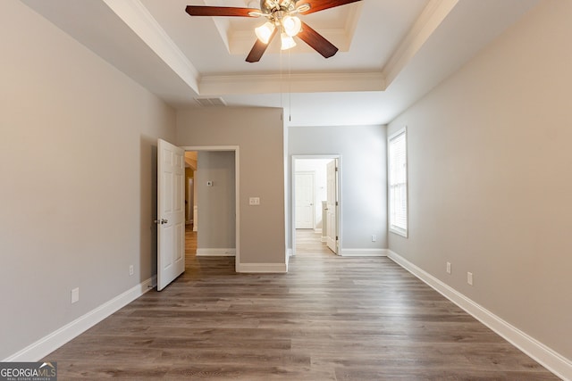 unfurnished bedroom with a tray ceiling, wood-type flooring, ornamental molding, and ceiling fan