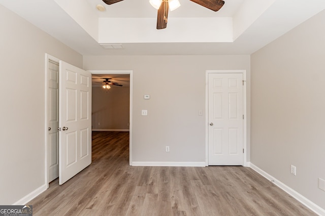 unfurnished bedroom with a raised ceiling, ceiling fan, and light wood-type flooring