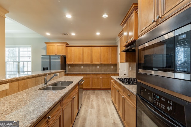 kitchen featuring sink, appliances with stainless steel finishes, light stone counters, tasteful backsplash, and light hardwood / wood-style floors