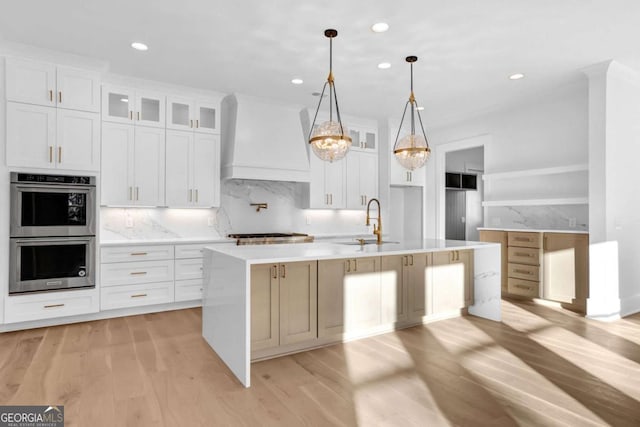 kitchen featuring white cabinetry, appliances with stainless steel finishes, custom range hood, and a kitchen island with sink