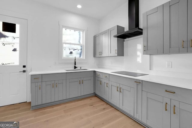 kitchen with sink, wall chimney range hood, gray cabinets, black electric cooktop, and light wood-type flooring