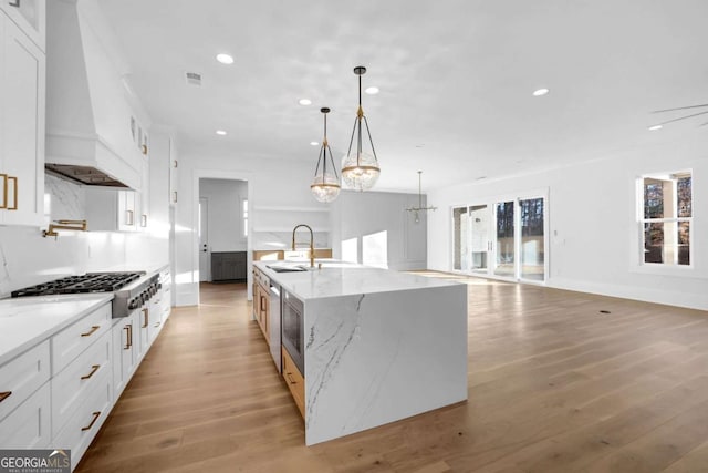 kitchen with a spacious island, light stone counters, white cabinets, decorative light fixtures, and stainless steel gas stovetop