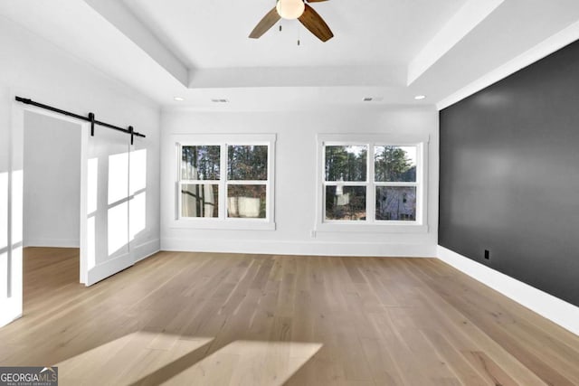 interior space with a barn door, ceiling fan, a tray ceiling, and light hardwood / wood-style flooring