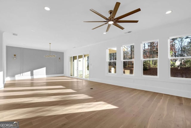 unfurnished living room featuring ceiling fan with notable chandelier and light wood-type flooring