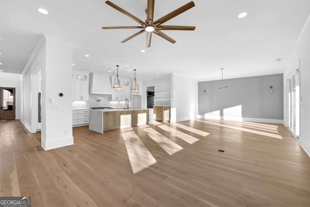 unfurnished living room featuring crown molding, sink, ceiling fan, and light wood-type flooring