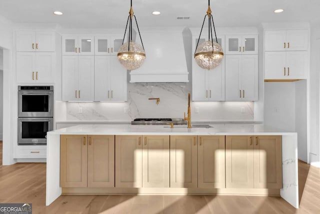 kitchen featuring premium range hood, pendant lighting, double oven, backsplash, and a center island with sink